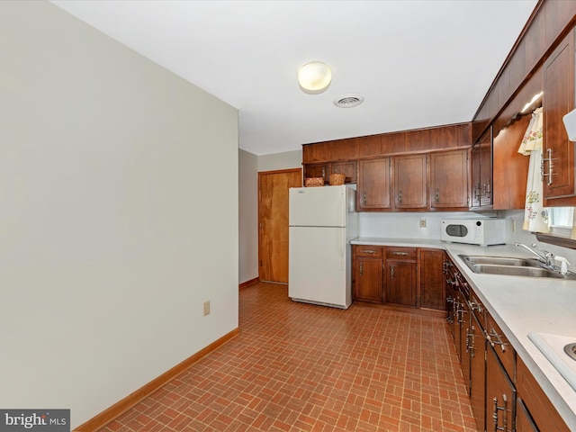 kitchen featuring baseboards, brick patterned floor, a sink, light countertops, and white appliances
