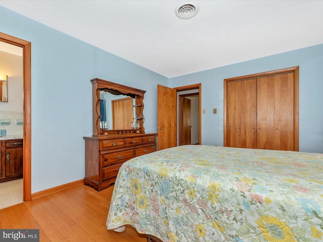 bedroom with ensuite bathroom, a closet, visible vents, light wood finished floors, and baseboards
