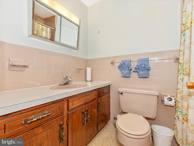 full bath featuring toilet, tile walls, vanity, and a wainscoted wall