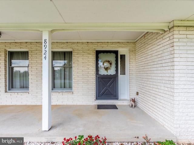 entrance to property featuring a porch and brick siding
