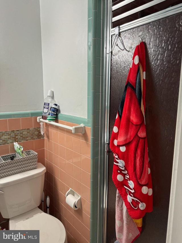 bathroom with a shower with door, toilet, and tile walls