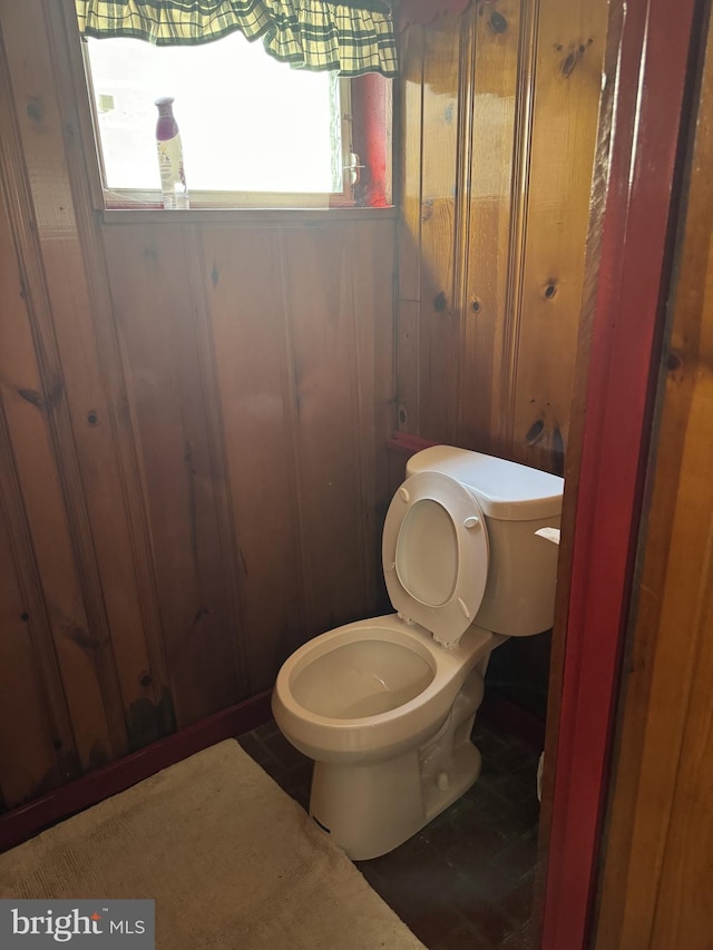 bathroom featuring wooden walls, toilet, and a healthy amount of sunlight