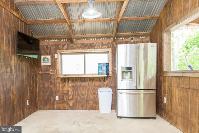 kitchen with concrete floors, wood walls, a wealth of natural light, and stainless steel fridge with ice dispenser