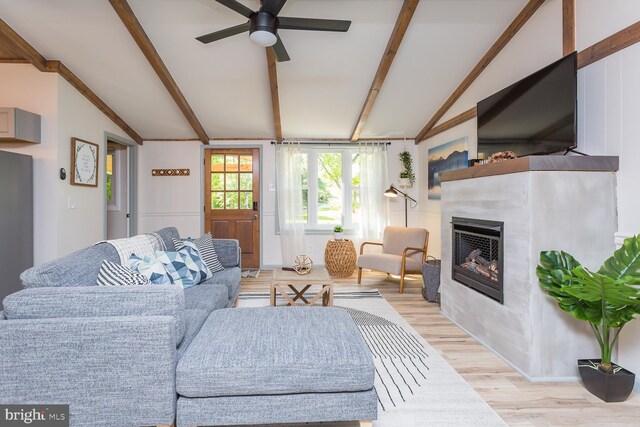 living room with a glass covered fireplace, ceiling fan, lofted ceiling with beams, and light wood-style flooring