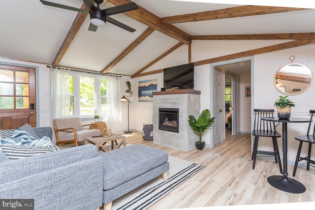 living area with a ceiling fan, plenty of natural light, light wood-style flooring, and vaulted ceiling with beams