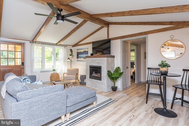 living area featuring a fireplace, a ceiling fan, vaulted ceiling with beams, and plenty of natural light