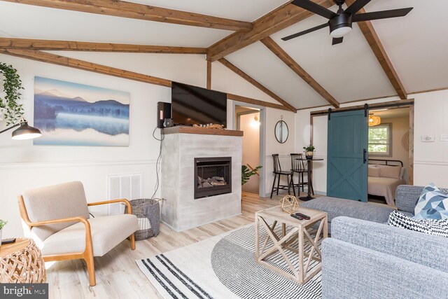 living room with a barn door, vaulted ceiling with beams, a ceiling fan, visible vents, and wood finished floors