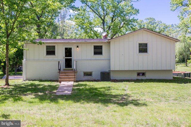 view of front facade with central AC, board and batten siding, entry steps, and a front lawn