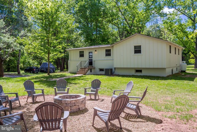 back of house with a lawn, cooling unit, an outdoor fire pit, and board and batten siding