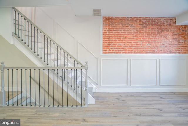 stairs with brick wall and hardwood / wood-style floors