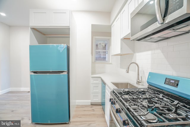 kitchen featuring appliances with stainless steel finishes, sink, backsplash, white cabinetry, and light hardwood / wood-style flooring