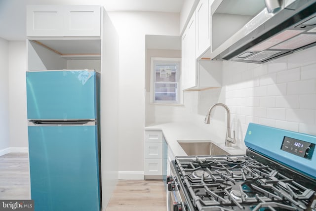 kitchen with gas stove, white cabinets, light wood-type flooring, stainless steel refrigerator, and sink