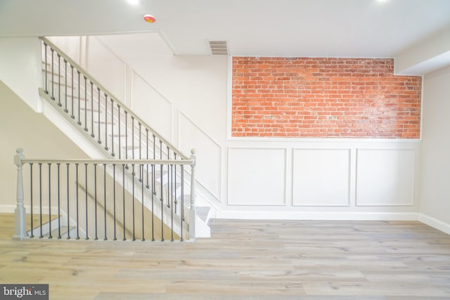 staircase with hardwood / wood-style floors and brick wall