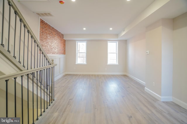 unfurnished room featuring brick wall and light hardwood / wood-style floors