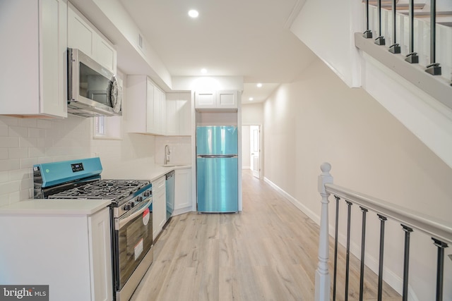 kitchen with backsplash, sink, light wood-type flooring, white cabinetry, and appliances with stainless steel finishes