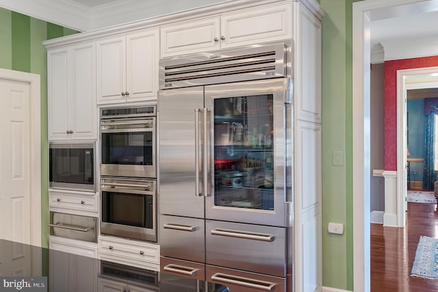 kitchen featuring white cabinetry, ornamental molding, built in appliances, and dark hardwood / wood-style flooring