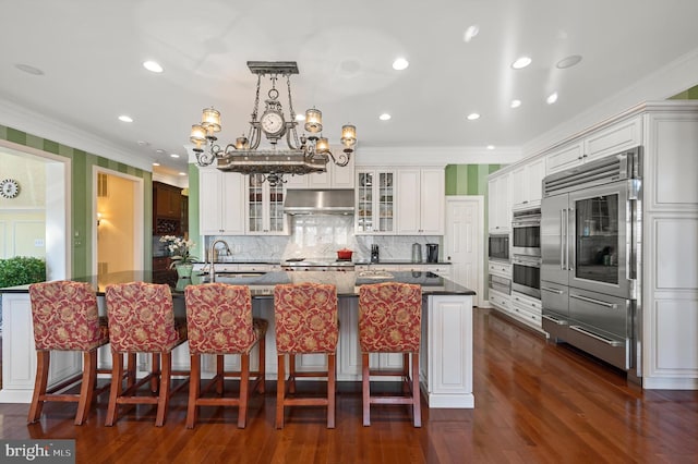 kitchen with under cabinet range hood, an inviting chandelier, a sink, crown molding, and glass insert cabinets