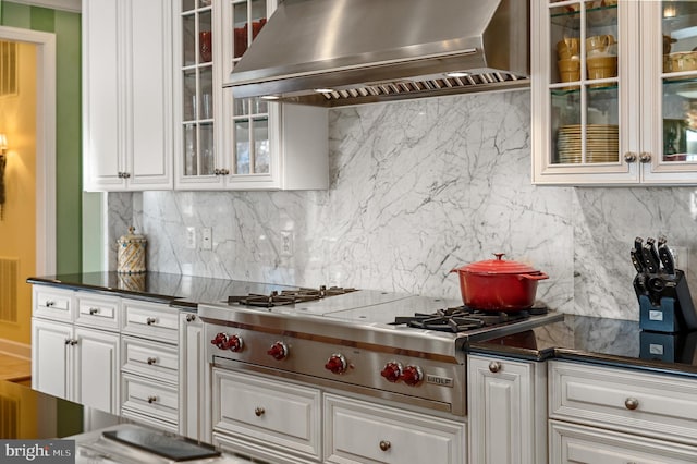 kitchen featuring wall chimney range hood, dark countertops, stainless steel gas cooktop, decorative backsplash, and white cabinetry