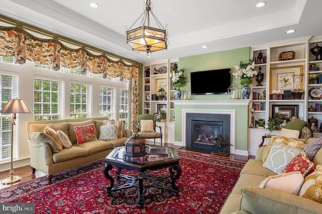 living room with crown molding, wood-type flooring, a raised ceiling, and built in shelves