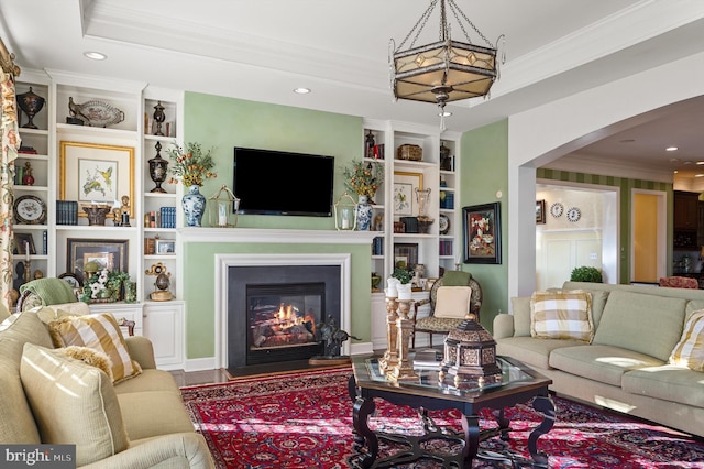 living room with built in shelves, a fireplace with flush hearth, arched walkways, ornamental molding, and recessed lighting