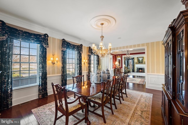 dining room featuring a notable chandelier, wallpapered walls, a wainscoted wall, ornamental molding, and visible vents