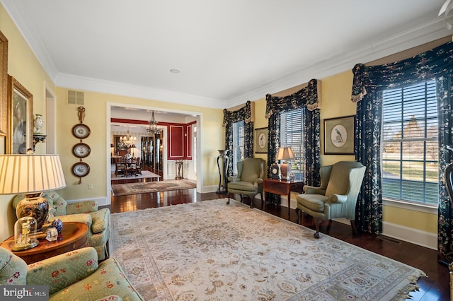 living room featuring crown molding, wood finished floors, baseboards, a notable chandelier, and visible vents