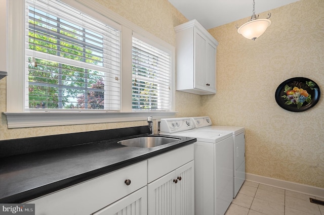 washroom featuring washing machine and clothes dryer, a sink, baseboards, wallpapered walls, and cabinet space
