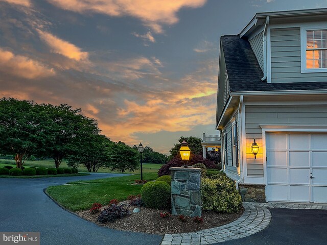 property exterior at dusk with a garage, a lawn, and a shingled roof