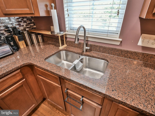 kitchen featuring dark stone countertops, light hardwood / wood-style floors, backsplash, and sink