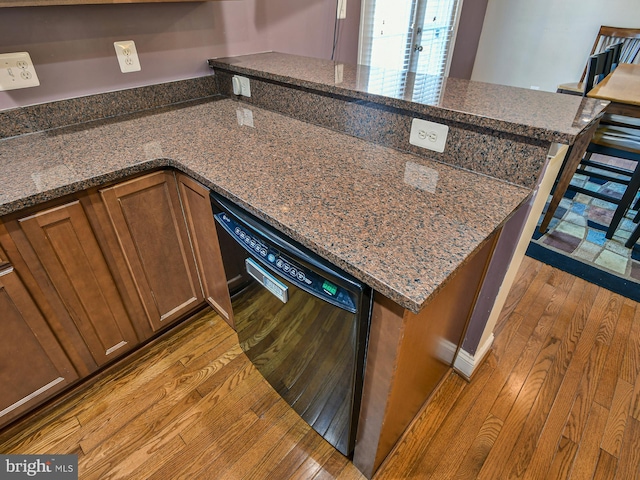 kitchen with dark stone counters, black dishwasher, and light hardwood / wood-style floors