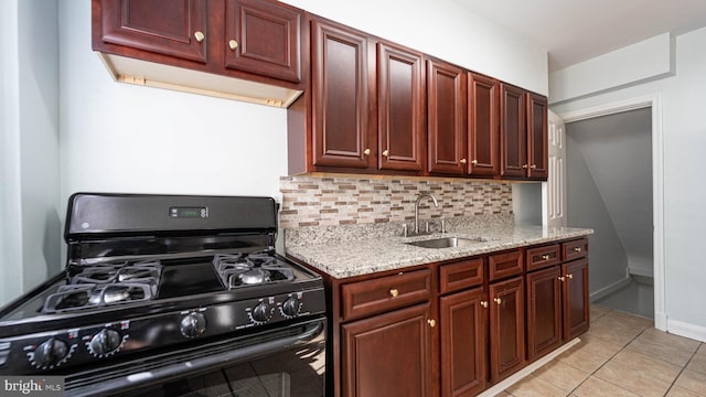 kitchen featuring light tile patterned floors, backsplash, light stone countertops, black range with gas stovetop, and sink