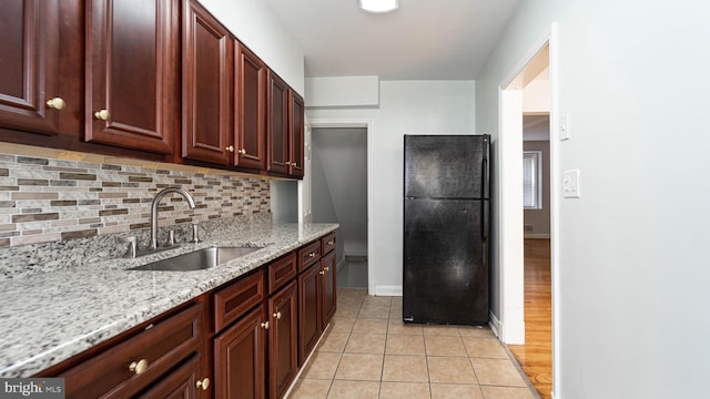 kitchen featuring decorative backsplash, black fridge, light hardwood / wood-style flooring, sink, and light stone counters