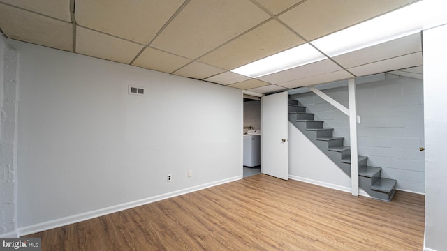 basement featuring a drop ceiling, light wood-type flooring, and washer / clothes dryer