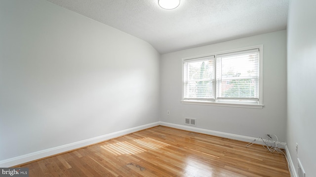 spare room featuring hardwood / wood-style flooring, a textured ceiling, and vaulted ceiling