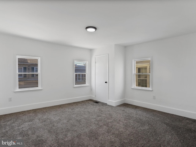 empty room featuring baseboards and dark colored carpet