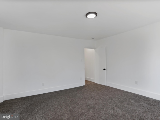 empty room featuring dark colored carpet and baseboards