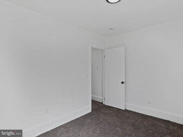 spare room with dark colored carpet and baseboards