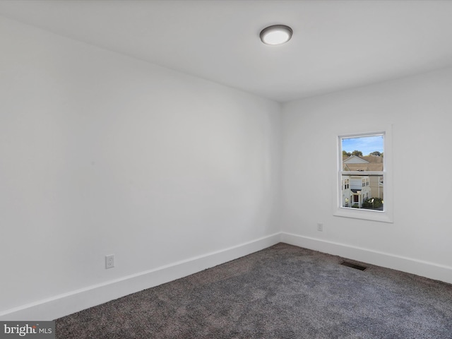 unfurnished room featuring baseboards, dark colored carpet, and visible vents