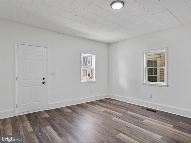 empty room featuring visible vents, baseboards, and dark wood-style floors