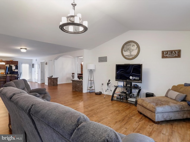 living room featuring hardwood / wood-style floors, vaulted ceiling, a notable chandelier, and ornate columns