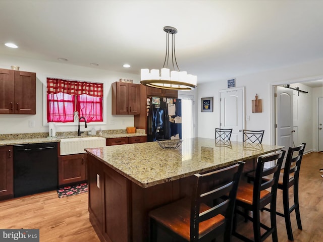 kitchen with a kitchen breakfast bar, a sink, light wood-style floors, a kitchen island, and black appliances