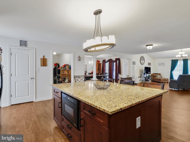 kitchen with black microwave, light stone counters, a kitchen island, light hardwood / wood-style floors, and decorative light fixtures