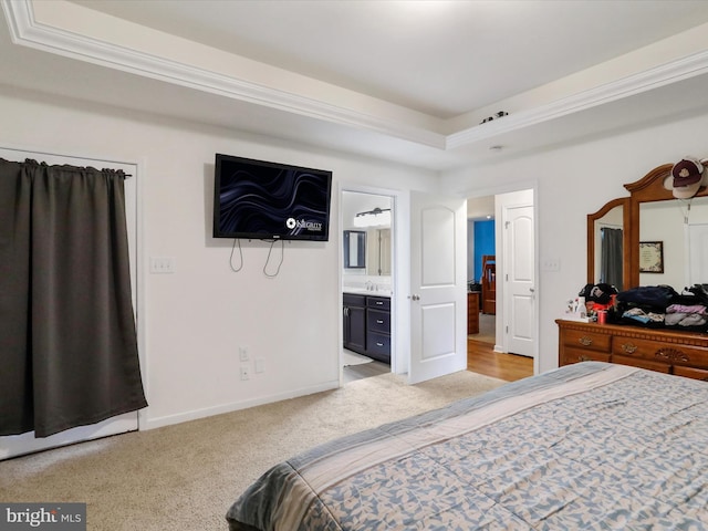 bedroom with connected bathroom, a sink, light colored carpet, a tray ceiling, and baseboards