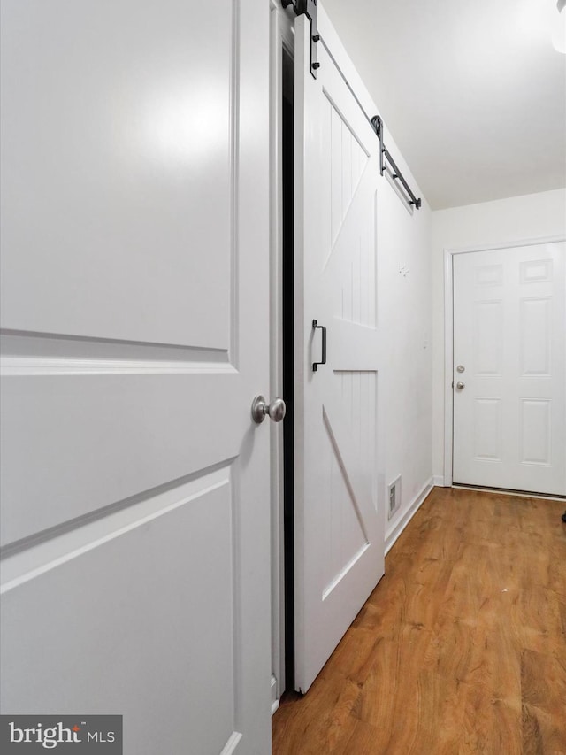 corridor with light wood finished floors, visible vents, a barn door, and baseboards
