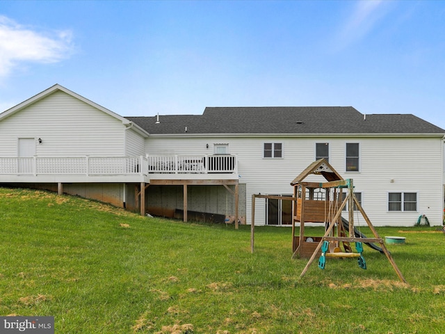 back of property featuring roof with shingles, a wooden deck, a playground, and a lawn