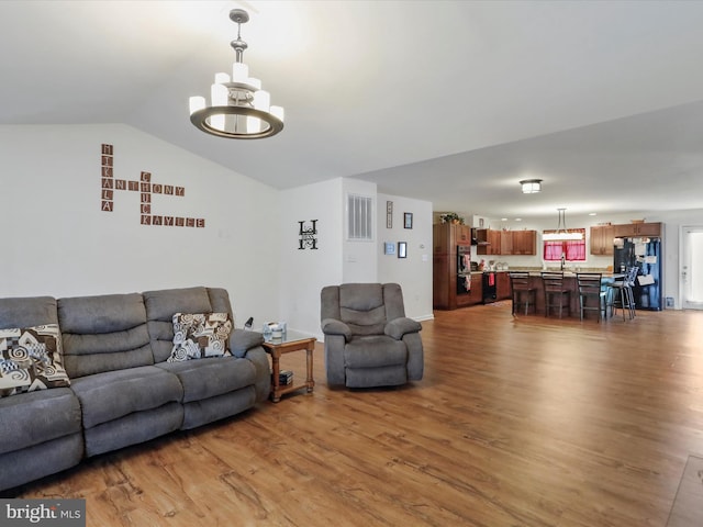 living area with wood finished floors, a notable chandelier, and lofted ceiling