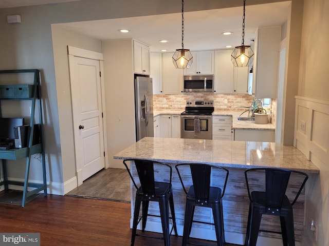 kitchen featuring appliances with stainless steel finishes, white cabinetry, light stone countertops, dark wood-type flooring, and decorative light fixtures