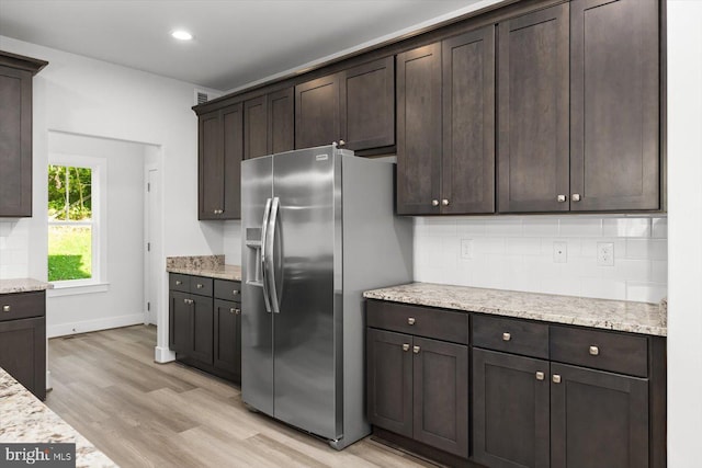 kitchen featuring light hardwood / wood-style flooring, dark brown cabinets, light stone counters, backsplash, and stainless steel fridge with ice dispenser