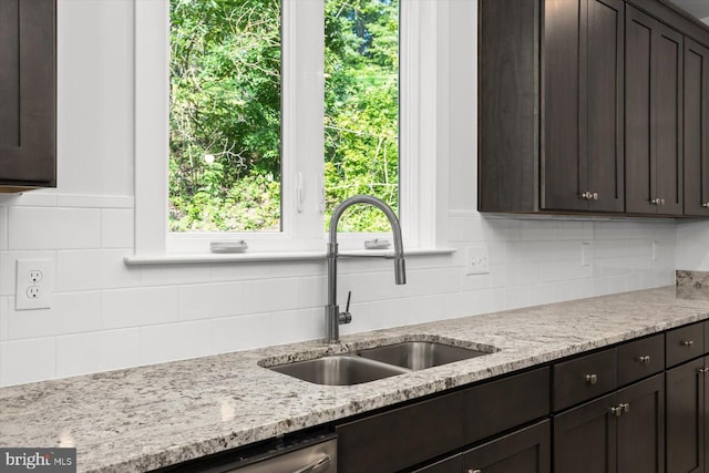 kitchen featuring tasteful backsplash, dark brown cabinets, light stone counters, and sink