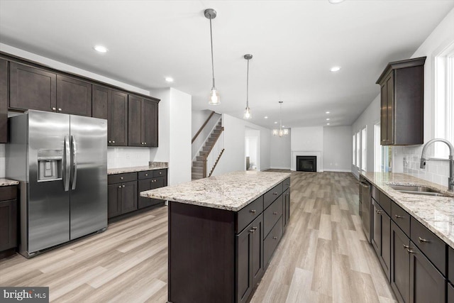 kitchen with light wood-type flooring, a kitchen island, decorative light fixtures, sink, and stainless steel appliances